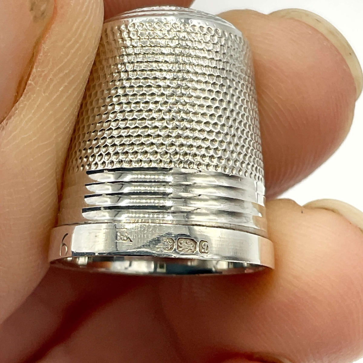 Silver thimble held between fingers against a white background
