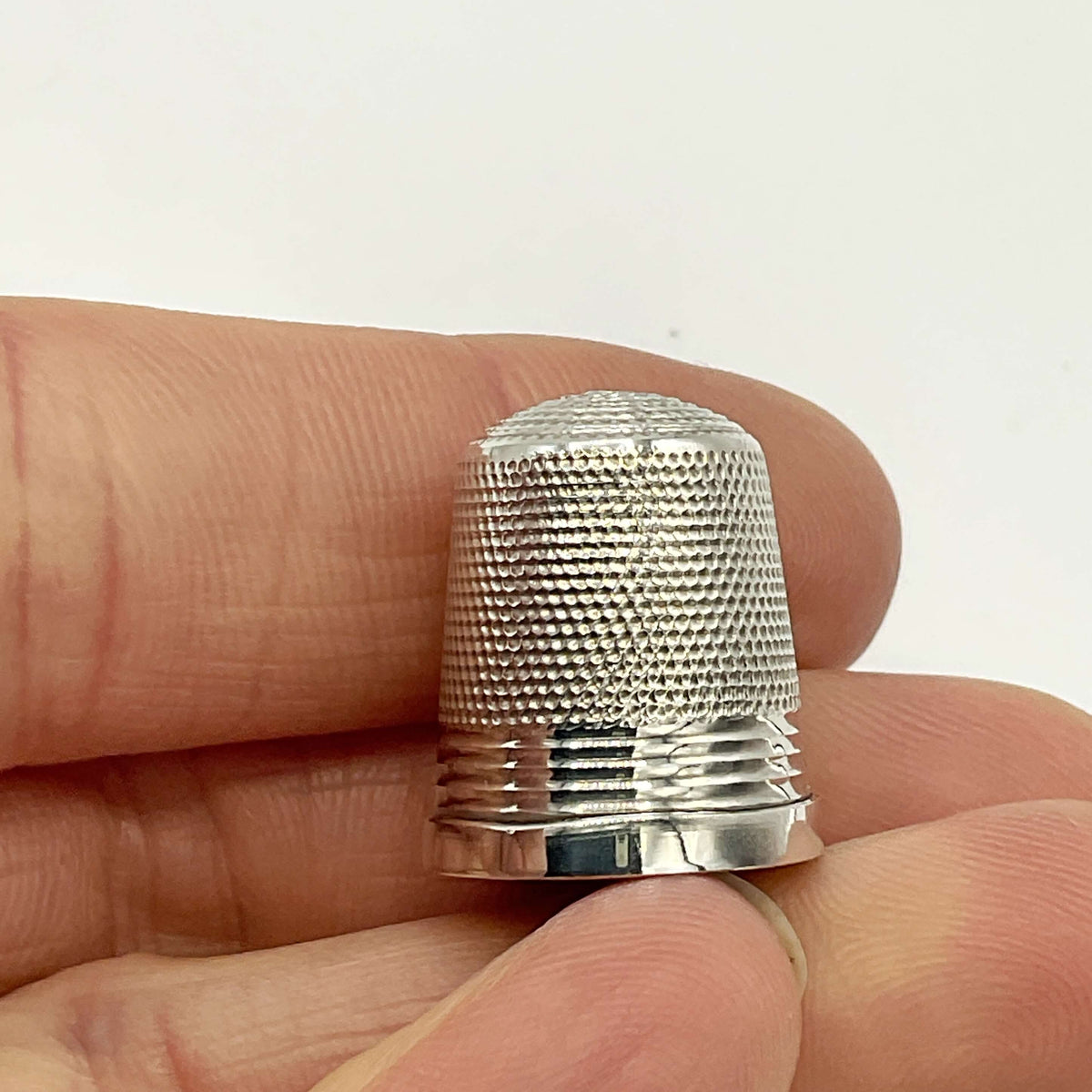 Silver thimble held between fingers against a white background