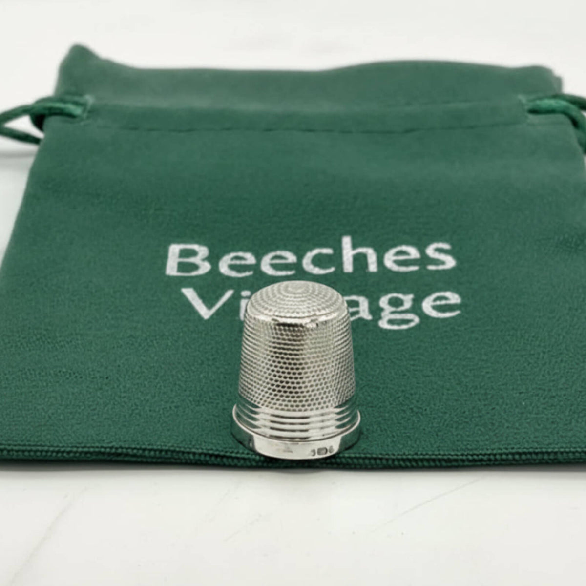 Silver thimble on a green cloth with 'Beeches Vintage' branding.