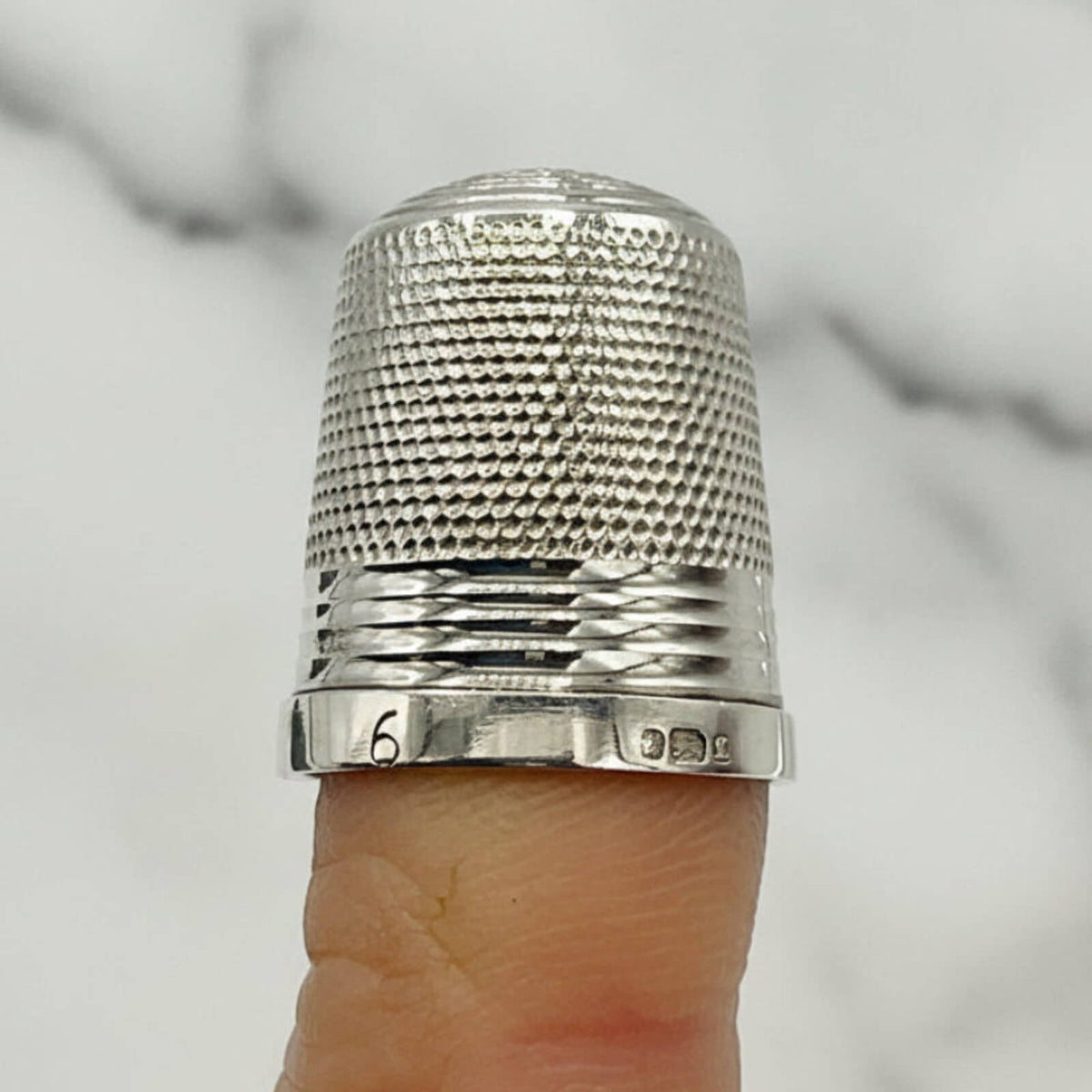 Silver thimble on a finger with a blurred background