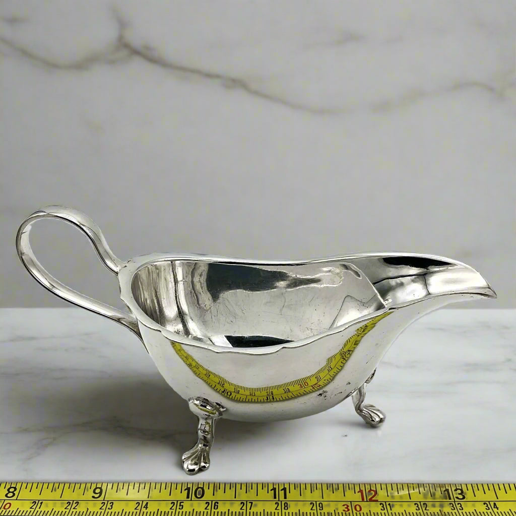 silver plated gravy boat next to a tape measure on a marble surface