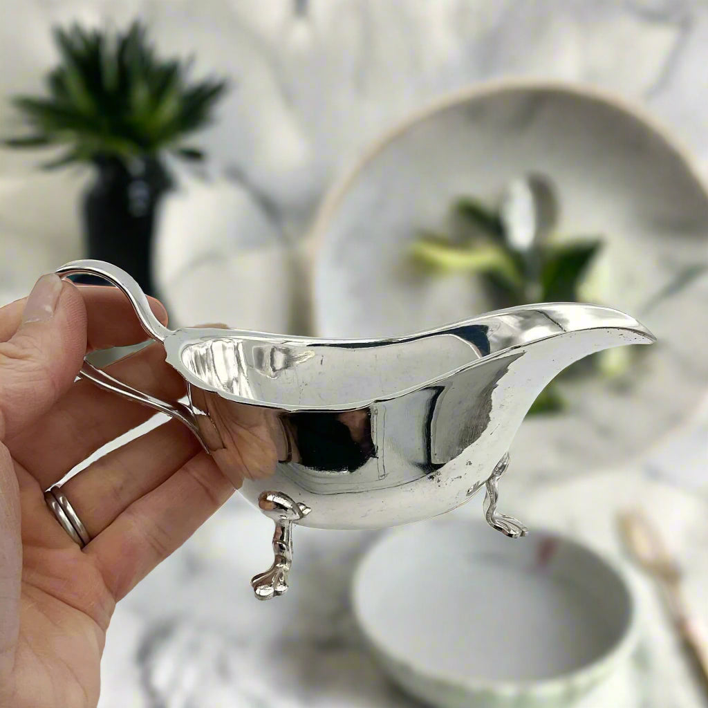 silver plated gravy boat with a table and plates in the background
