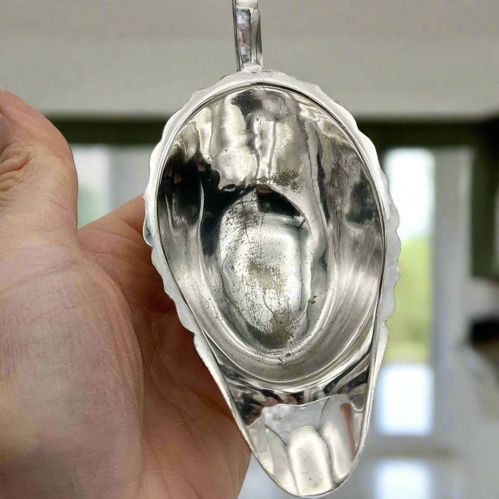 inside of silver plated gravy boat  held in a hand with kitchen windows in the background