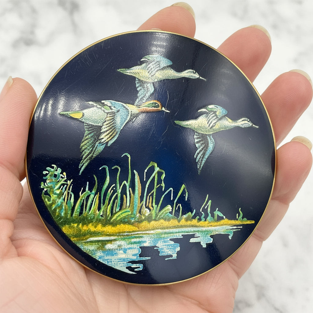 beautiful enamel featuring three ducks flying over water on a mirror compact lid held in a hand with a marble background