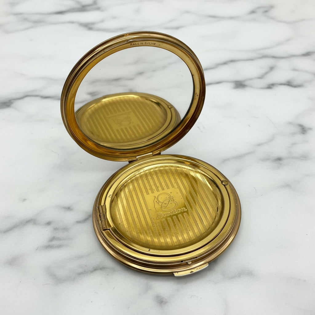 open powder compact lid showing clear mirror and a Stratton branded inner lid on a marble surface