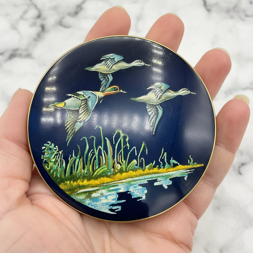 beautiful enamel featuring three ducks flying over water on a mirror compact lid held in a hand with a marble background