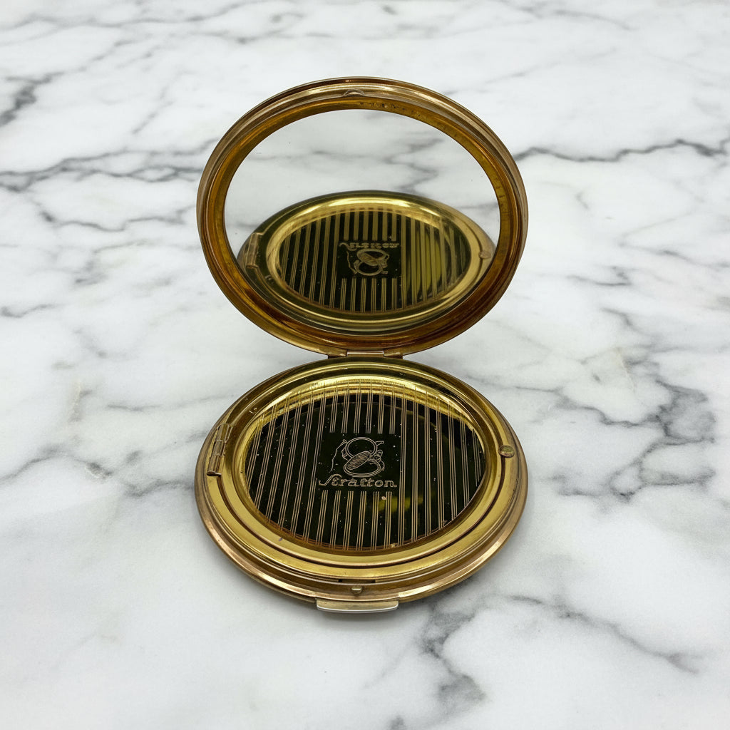 open powder compact showing a clear mirror and Stratton inner lid on a marble surface
