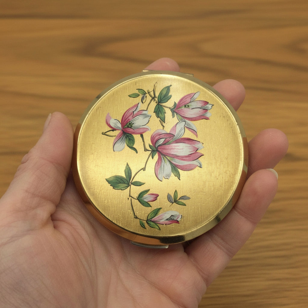 pretty gold compact with flowers on lid held in a hand with wood background