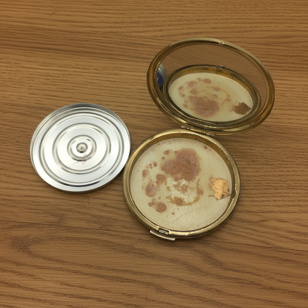 inside of Stratton mirror compact showing a relective mirror and a powder base to one side on wood
