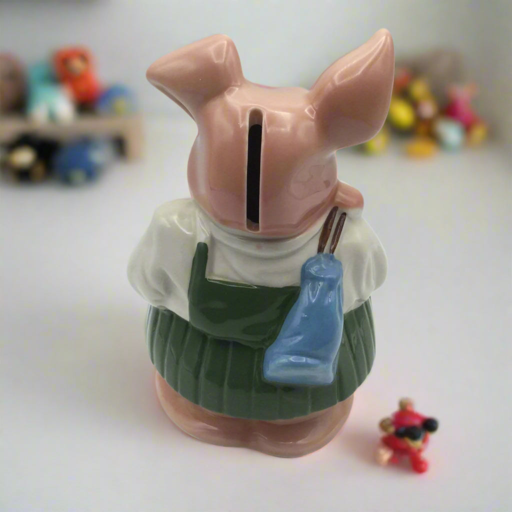 Annabel piggy bank back view on a white table with toys around it