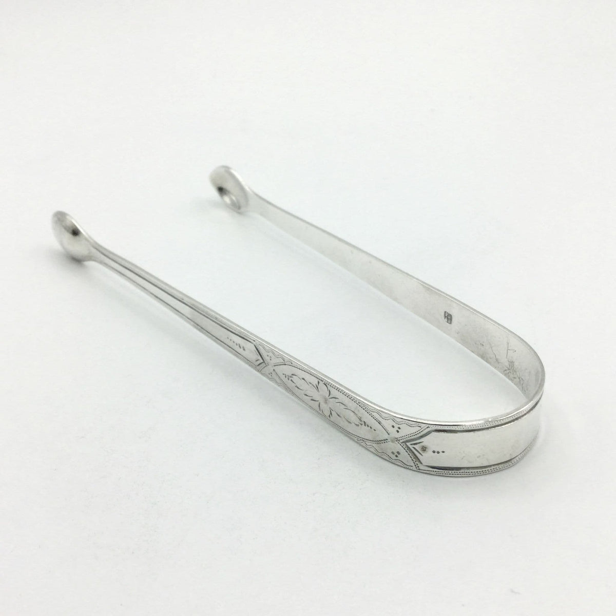 1700s Silver sugar tongs with a pretty floral engraved design on a white background