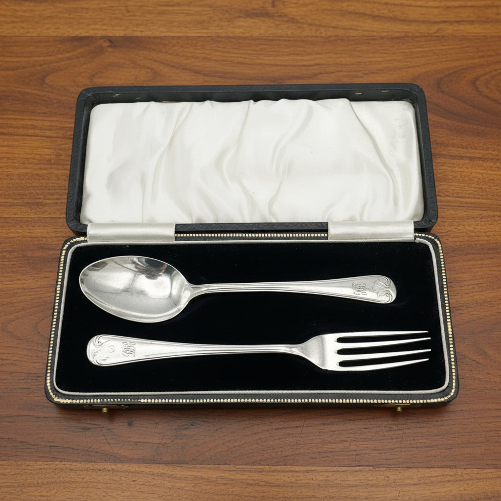 A matching silver spoon and fork sitting in a black presentation box on wood table