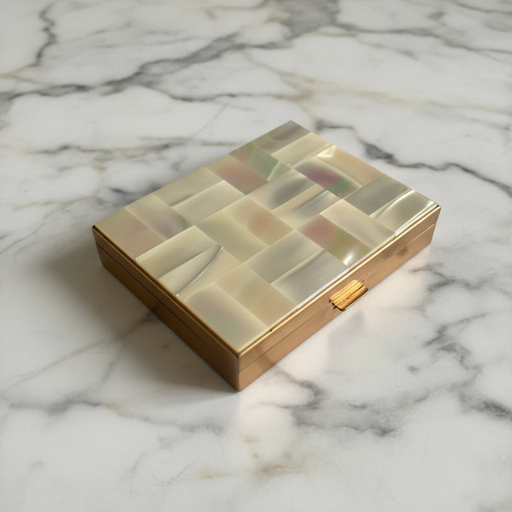 A musical compact sitting on a white background. The lid is decorated with rectangular pieces of Mother of Pearl shell and the sides of the compact are gold coloured.