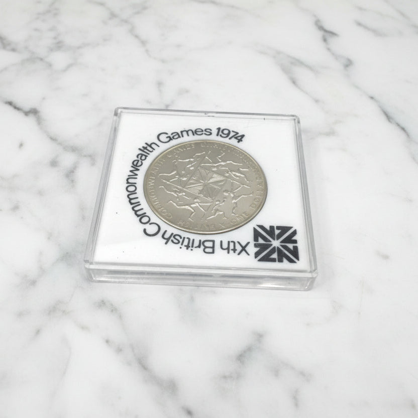 One dollar coin in a white case with 10th British Commonwealth Games 1974 around it.