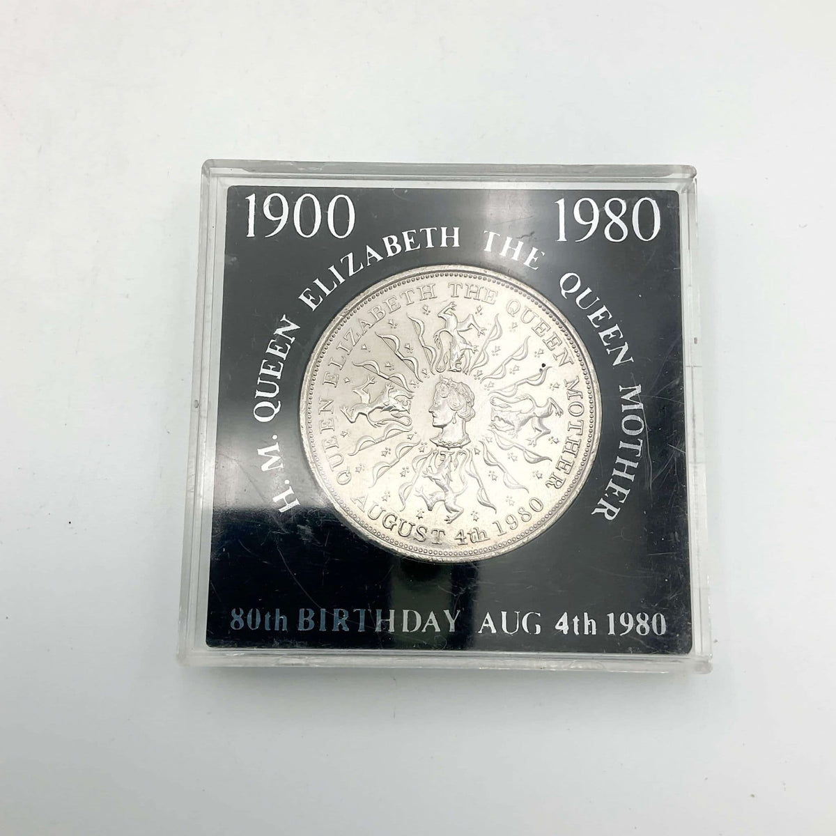 Silver coin with Queen Mother's head in the centre in a black case