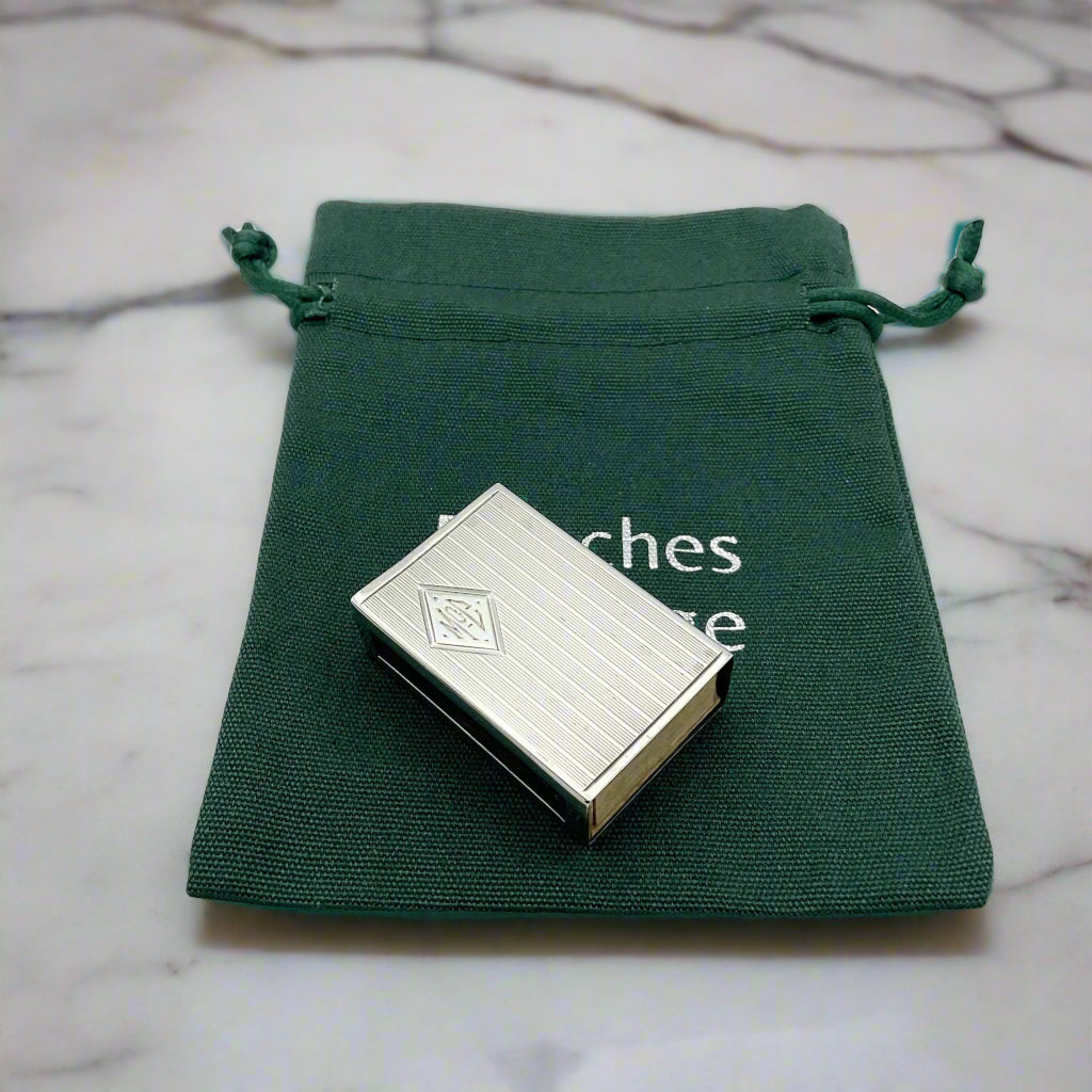 Vintage sterling silver matchbox holder with a diamond cartouché engraved with 'Sterling' and the brand mark '5056 JE Caldwell & Co', presented in a green velvet-lined presentation bag.on marble