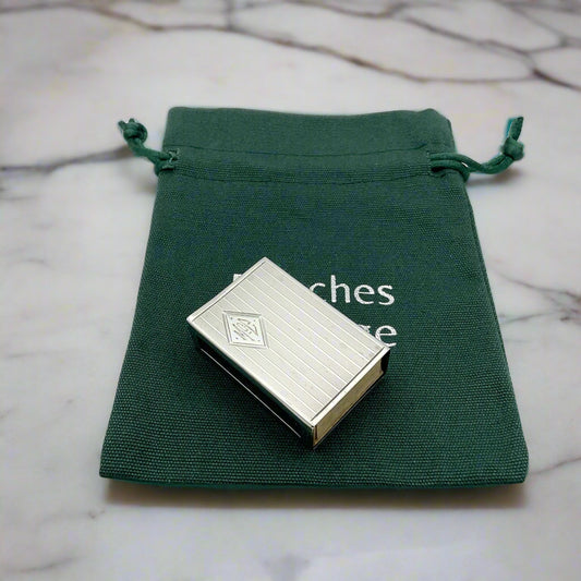 Vintage sterling silver matchbox holder with a diamond cartouché engraved with 'Sterling' and the brand mark '5056 JE Caldwell & Co', presented in a green velvet-lined presentation bag.on marble