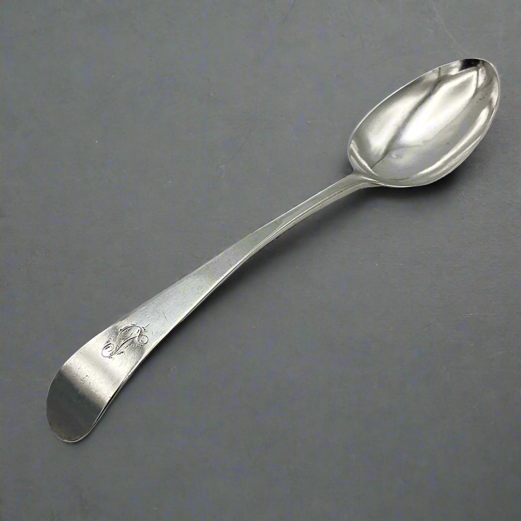 Antique silver serving spoon with an L engraved on the handle on a grey background