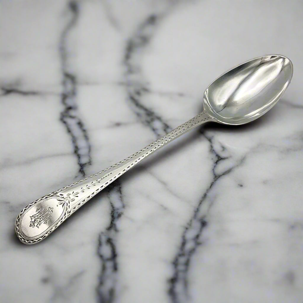 Large antique silver serving spoon with an engraved handle on a marble worktop