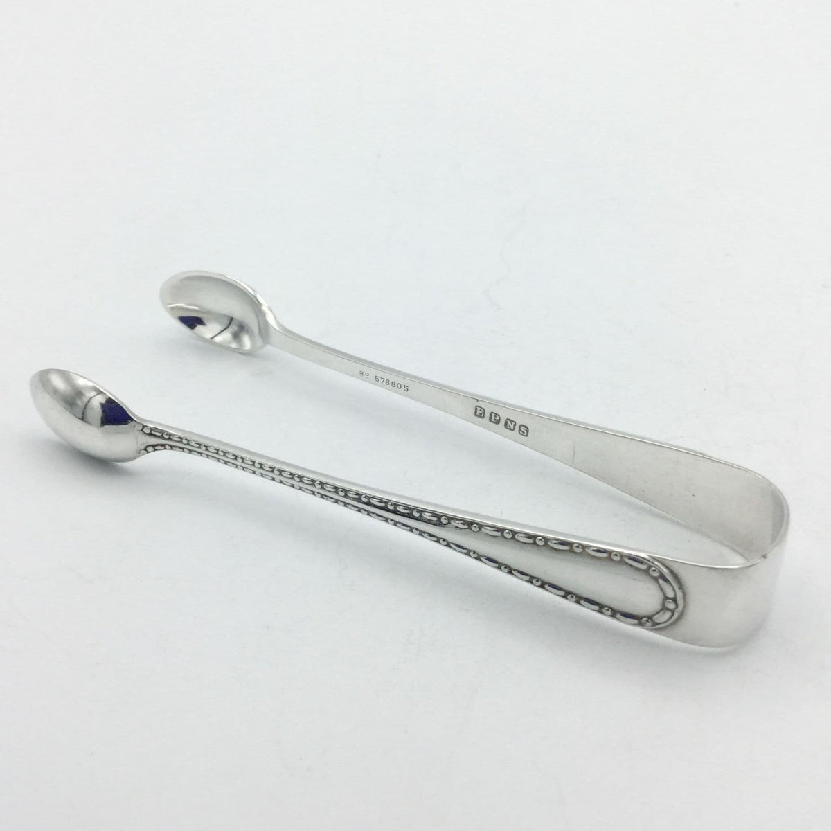 silver plated sugar tongson a white background with a dash pattern on it's arm and EPNS on the inside
