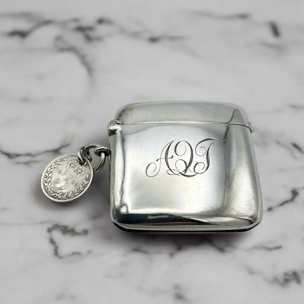 Silver vesta case with monogram and Threepence coin attached on a marble background