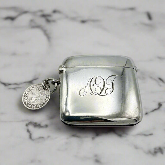 Silver vesta case with monogram and Threepence coin attached on a marble background