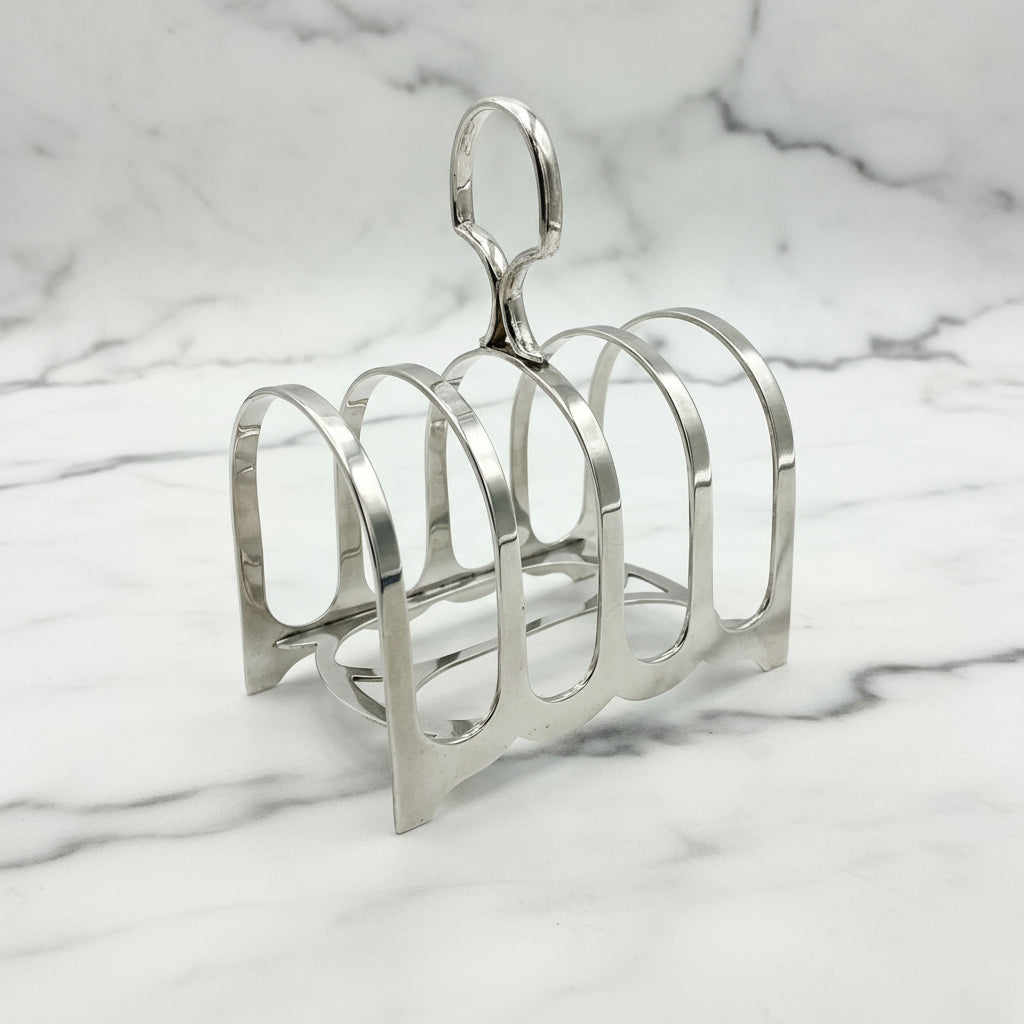 Antique sterling silver toast rack with five curved arches and a loop handle at the top, placed on a marble background.