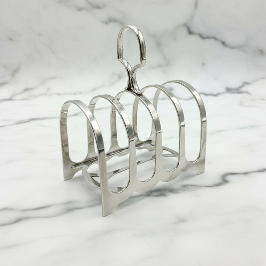 Antique sterling silver toast rack with five curved arches and a loop handle at the top, placed on a marble background.