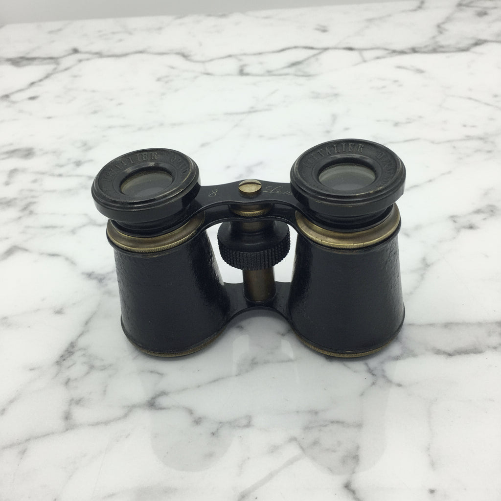 Black binoculars with brass accents on a marble surface