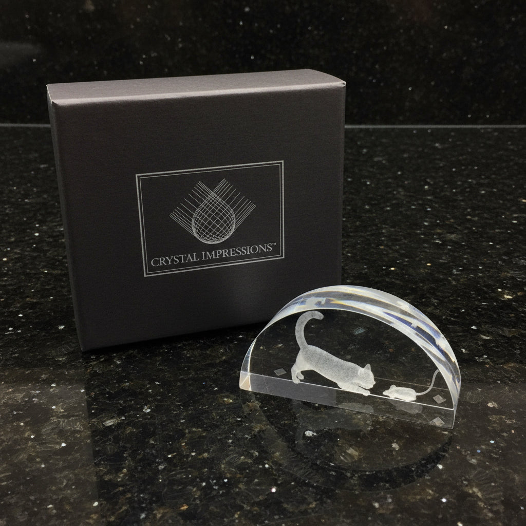 Crystal paperweight with cat and mouse design in front of Crystal Impressions box on a dark surface