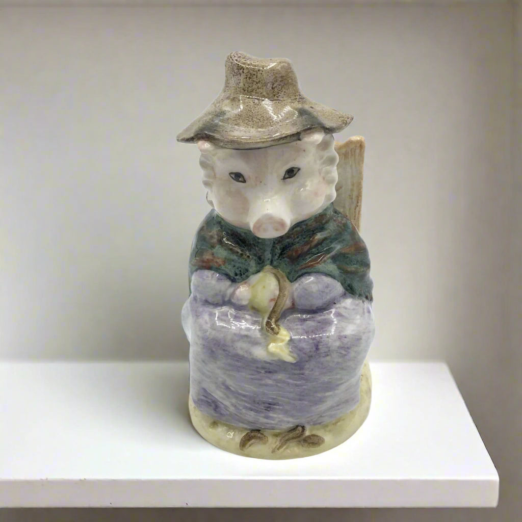 A figurine of a pig wearing a mauve dress and a green and brown shawl, sitting on a chair with a hat on, on a white shelf.