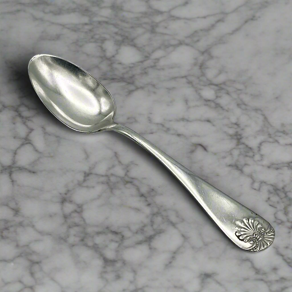 Antique silver-plated spoon with a Benjamin Franklin design on the handle, showing light scratches and a bit of tarnish. on a marble worktop