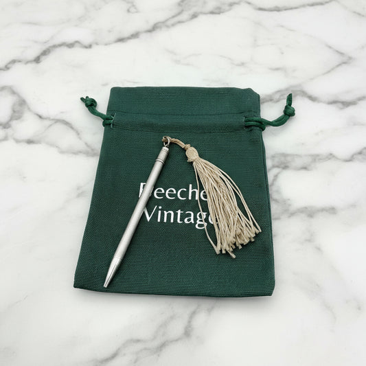 A vintage sterling silver propelling pencil with a beige tassel, displayed in a green gift bag with the text 'BEECHES VINTAGE' on it on marble